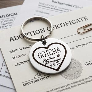 May include: A circular silver-toned metal keychain featuring an engraved heart outline. Inside the heart, the text reads GOTCHA, followed by the names Steven & Brianna and the date 6.6.18. The keychain includes a standard split ring attachment.