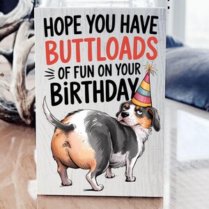 May include: A humorous birthday card featuring a cartoon dog wearing a party hat with the text "Hope you have buttloads of fun on your birthday."