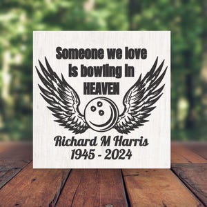 May include: A white wooden sign with black text and a bowling ball design with wings. The text reads "Someone we love is bowling in HEAVEN" and includes the name "Richard M Harris" and the years "1945 - 2024".