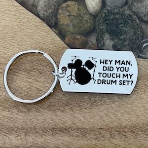 May include: A silver keychain with a black silhouette of a drum set and the text "Hey man, did you touch my drum set?"