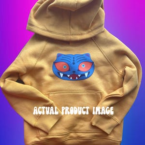 May include: Mustard yellow hoodie with a blue cat graphic featuring red eyes and white teeth. The hoodie has a hood and a front pocket. The text "ACTUAL PRODUCT IMAGE" is printed across the front.
