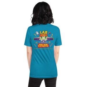 Op de afbeelding: Een turquoise t-shirt met de tekst "LAB STORY" in geel, rood en groen, samen met de zin "IN FINITY AND BEYOND" en "FOR OUR PATIENTS!" in het wit. Het shirt heeft verschillende medische afbeeldingen.