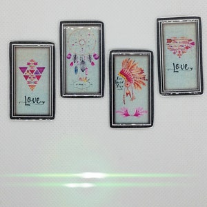 May include: Four rectangular pendants with silver-colored frames. Each pendant features a different design on a light blue background. Designs include a dreamcatcher, a Native American headdress, a geometric pattern, and an arrow heart. The word "Love" appears on two pendants.