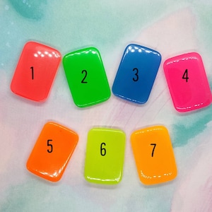 May include: Seven small, rectangular, brightly colored tiles with numbers 1 through 7 printed on them. The tiles are arranged in a semi-circle.