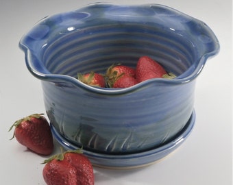 Könnte beinhalten: Ein blauer Keramiktopf mit einem gewellten Rand und einer passenden Untertasse. Der Topf ist mit roten Erdbeeren gefüllt.