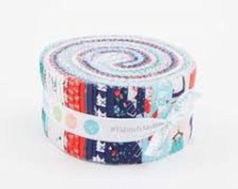 May include: A fabric roll featuring a variety of patterned fabric strips in shades of blue, red, and white. The roll is secured with a white ribbon and a label with text. The fabric appears to be cotton, suitable for quilting or crafting projects.