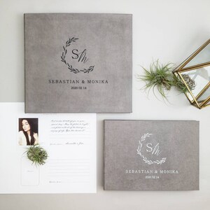 May include: Two gray photo albums with a white floral wreath and the initials "S&M" in the center. The text "Sebastian & Monika 2020 02 14" is printed below the wreath on each album.