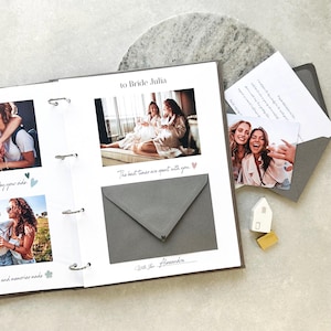 Puede incluir: Un álbum de recortes con páginas blancas, fotografías, un sobre gris y texto impreso que incluye "to Bride Julia", "The best times are spent with you" y "With love Alexandra". Una pequeña figura de casa blanca y un bloque dorado.