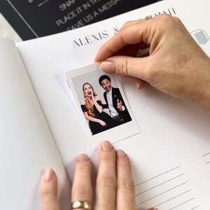 May include: A polaroid photo of a smiling couple is held over a blank page of a notebook. The notebook has the name "ALEXIS &" printed on it. The photo shows a woman with long blonde hair and a man in a suit.