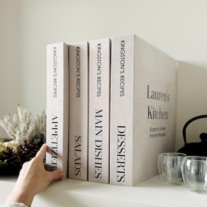 May include: Four off-white recipe books are displayed. The books are labelled "Appetizer", "Salads", "Main Dishes", and "Desserts". The fourth book is labelled "Lauren's Kitchen" and "Kingston's Family Favorite Recipes".