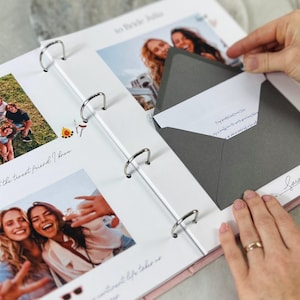 Puede incluir: Un álbum de recortes de anillas blanco con varias fotografías en color de personas, texto escrito a mano y un sobre gris oscuro pegado a la página. Las páginas del álbum contienen leyendas impresas e ilustraciones de una fogata.
