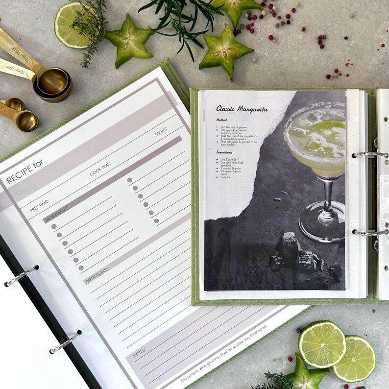 An opened recipe book page with a pink header that reads 'RECIPE for'. The recipe book page has sections for prep time, cook time, serves, ingredients, directions, and notes. And printed cocktail recipe from the internet as an example.