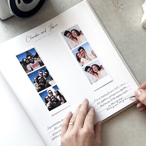 May include: A white wedding photo album with the names "Claudia and Jevce" and the date "JUNE 20.2025" printed on the top. The album contains photo strips and handwritten notes. A hand with a gold ring is writing on the page.