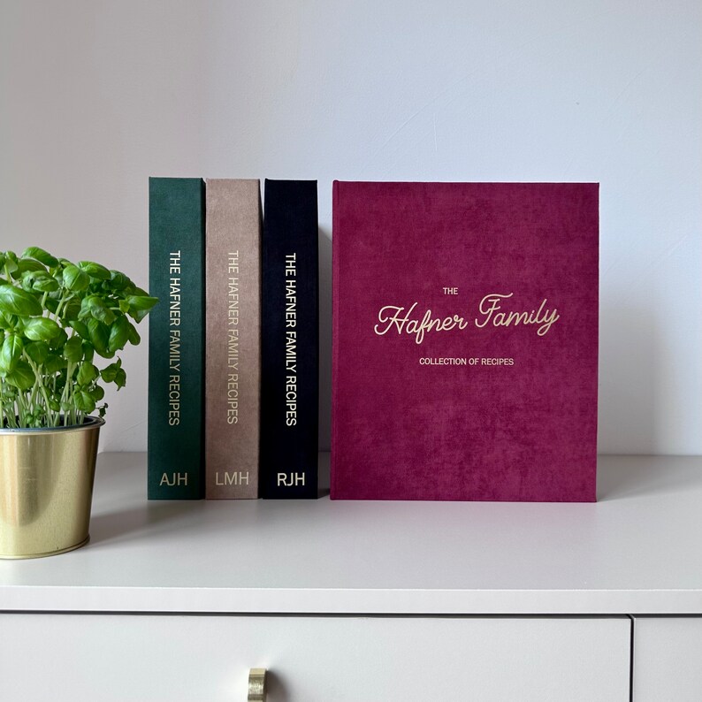 Four recipe book binders in the shelf. Binders are in Dark green, Taupe, Black and Burgundy colors with Foil gold lettering/text on the cover and spine.