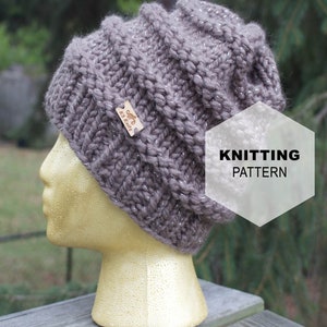 Könnte beinhalten: Eine graue Strickmütze mit silbernem Garn, das durch das gesamte Material gewebt ist. Die Mütze sitzt auf einem Mannequin-Kopf. Der Text "KNITTING PATTERN" befindet sich auf einem weißen Sechseck.
