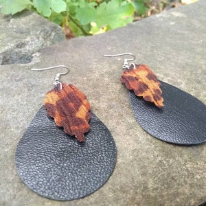 May include: A pair of black leather teardrop earrings with a brown and orange animal print accent.