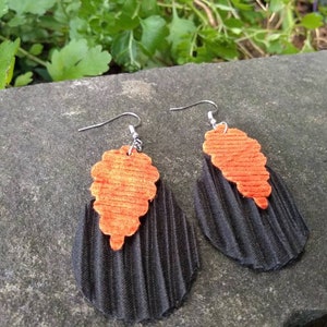 May include: A pair of black and orange earrings with a textured, pleated design. The earrings are made of fabric and have a silver hook closure.