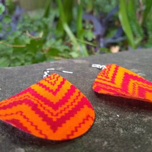 May include: A pair of orange and red fabric earrings with a chevron pattern. The earrings are teardrop shaped and have silver hooks.