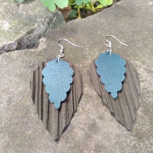 May include: A pair of dangle earrings with a dark gray, textured, leaf-shaped base and a teal blue, scalloped, grape-shaped top.
