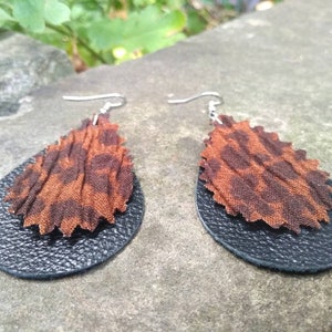 May include: A pair of dangle earrings with a black leather base and a brown and black patterned fabric top.