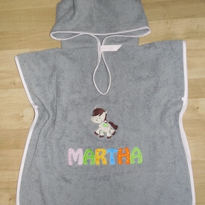 Könnte beinhalten: Grauer Kapuzenhandtuch mit rosa Saum und einem weißen Pferde-Applikationen. Das Handtuch hat den Namen "MARTHA" in bunten Buchstaben bestickt.