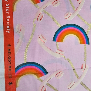 Puede incluir: Tela rosa con un patrón repetido de arcos iris y teléfonos de disco blanco con cordones dorados. La tela tiene el texto "2019 Ruby Star Society ©MELODY MILLER *" impreso en el lateral.