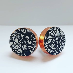 May include: A pair of round, black and white patterned earrings with copper backing.