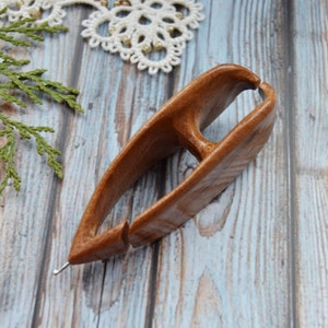 May include: A wooden knitting needle holder with a smooth, brown finish. The holder has a unique shape with a small opening at the top and a larger opening at the bottom. The holder is designed to hold knitting needles securely in place.