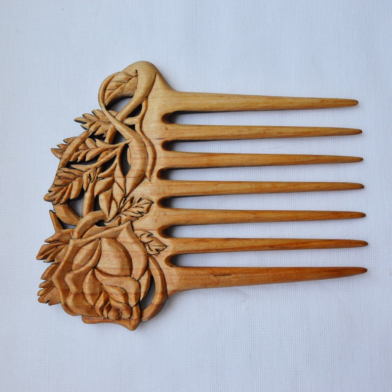 May include: A wooden comb with a carved rose design. The comb has seven teeth and is made of light brown wood.