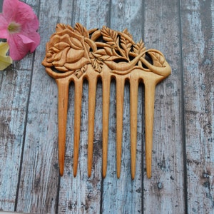 May include: A wooden hair comb with a carved rose design. The comb has seven teeth and is made of light brown wood.