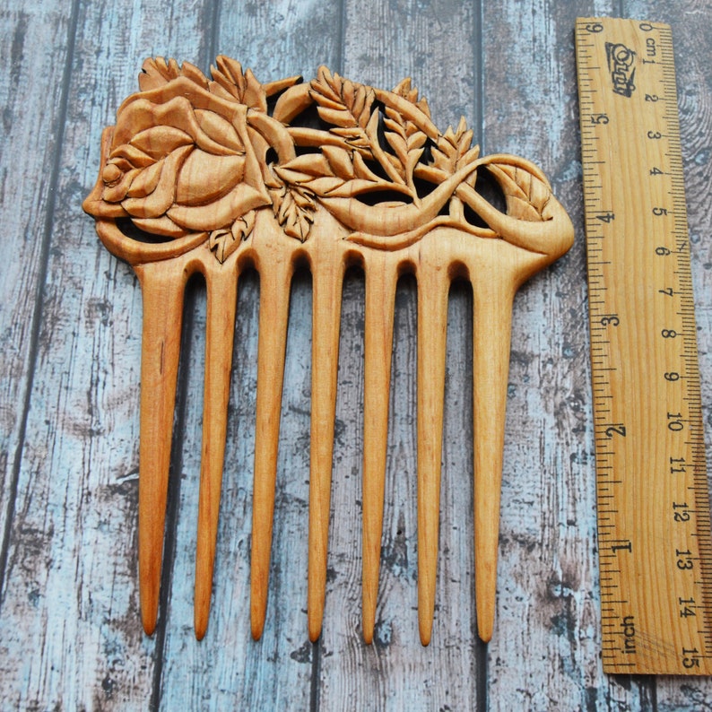 May include: A wooden comb with a carved rose design. The comb is approximately 5 inches long and has 7 teeth.