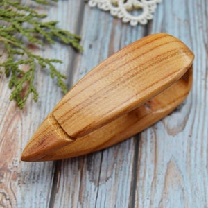 May include: A wooden clothespin with a natural finish. The clothespin is made of two pieces of wood that are joined together in the middle. The clothespin is designed to hold items together.