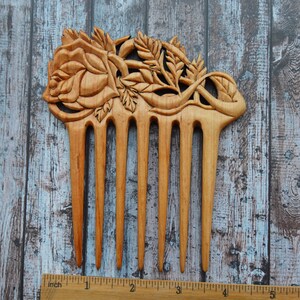 May include: A wooden comb with a carved rose design. The comb is approximately 5 inches long and has 7 teeth.