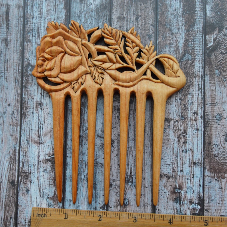May include: A wooden comb with a carved rose design. The comb is approximately 5 inches long and has 7 teeth.
