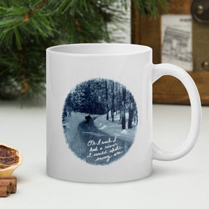 May include: White ceramic mug featuring a winter scene illustration in a blue circle. The image depicts a snowy road winding through a forest. The mug has the text "Oh I wish I had a river I could skate away on."