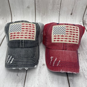 May include: Two distressed denim trucker hats with a red, white, and blue American flag design featuring a row of fish. One hat is gray and the other is red.