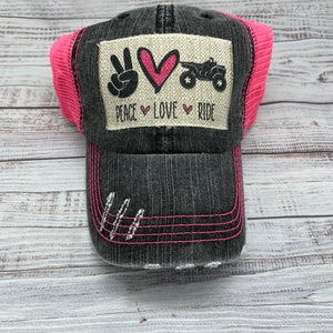May include: A black and pink trucker hat with a patch that says "Peace Love Ride" and a peace sign, heart, and ATV graphic.