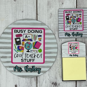 May include: A set of three teacher desk accessories featuring a round coaster, a square coaster, and a notepad with a sticky note. All three items have a gray and white striped background with a pink square in the center. The pink square has a graphic of school supplies and the text "Busy Doing Cool Teacher Stuff" and "Ms. Bailey".