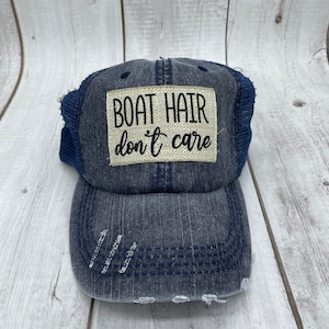 May include: A blue denim baseball cap with a distressed look and a beige patch that reads "BOAT HAIR don't care".