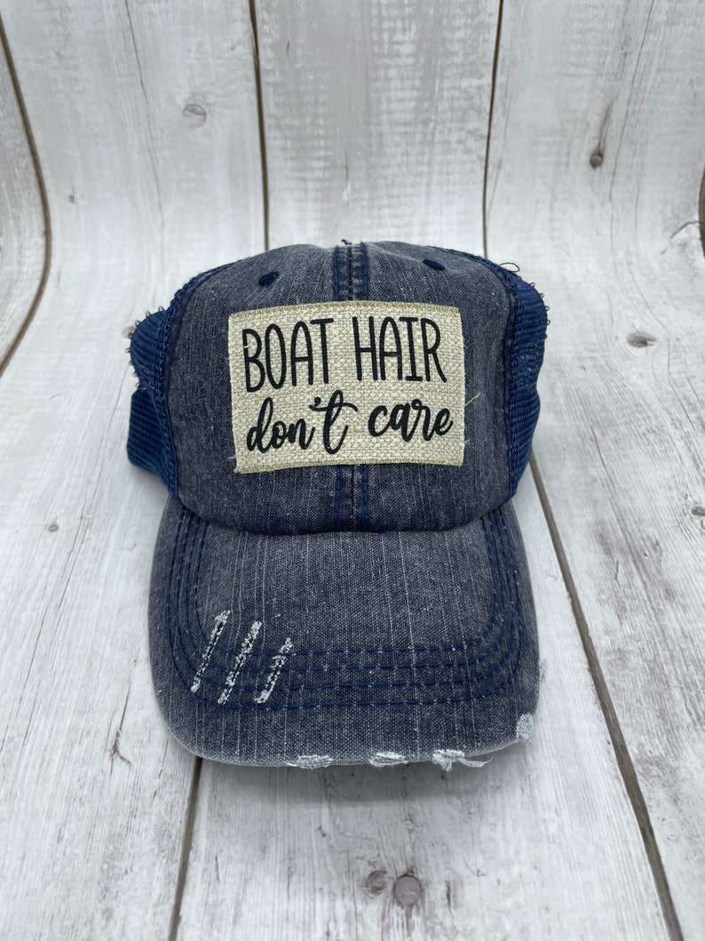 May include: A blue denim baseball cap with a distressed look and a beige patch that reads "BOAT HAIR don't care".
