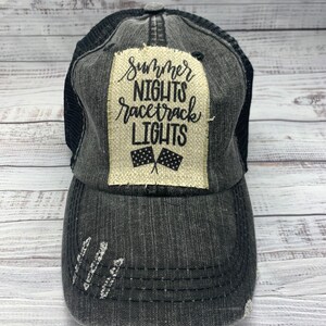May include: A black and gray distressed trucker hat with a beige patch that says "Summer Nights Racetrack Lights" with a black and white checkered flag graphic.