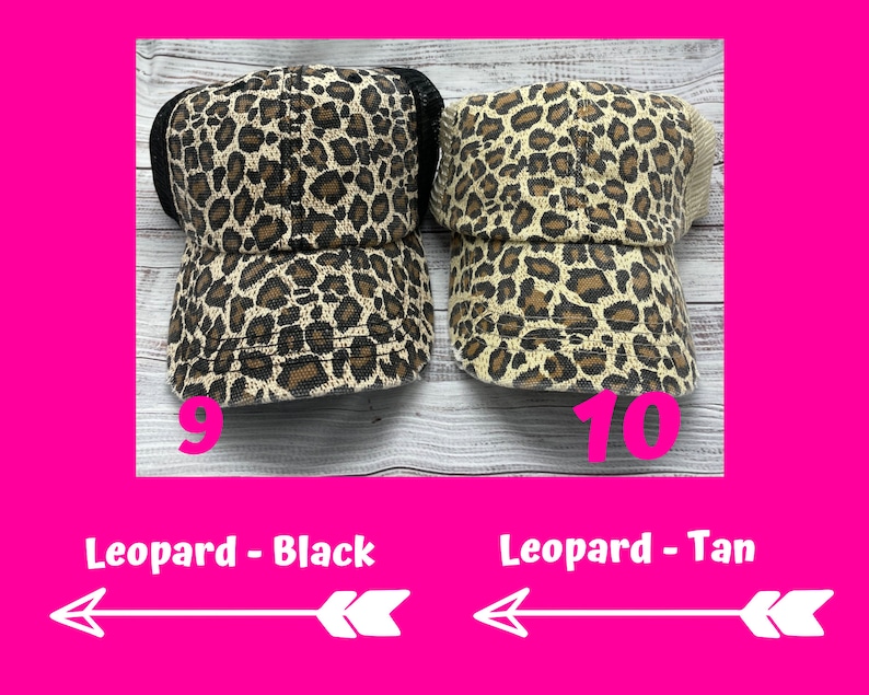 May include: Two leopard print trucker hats, one with a black mesh back and one with a tan mesh back. The hats are on a wooden surface. The text "Leopard - Black" and "Leopard - Tan" is below the hats.
