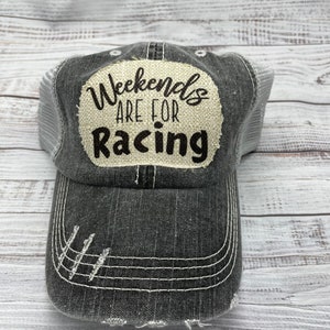 May include: A black and white distressed trucker hat with a beige patch that reads "Weekends Are For Racing".