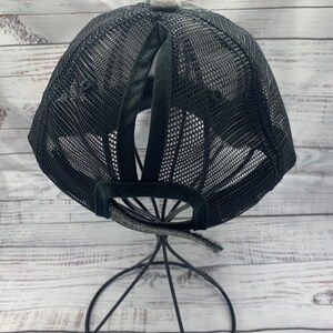 May include: Black mesh baseball cap with a ponytail hole in the back. The cap is on a black metal stand.