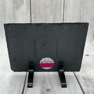 May include: Black slate plaque with a pink circle sticker that says "H&K Custom Creations, Shannon McDonald, Etsy Shop, Handmade with Love". The plaque is on a black stand with two legs.