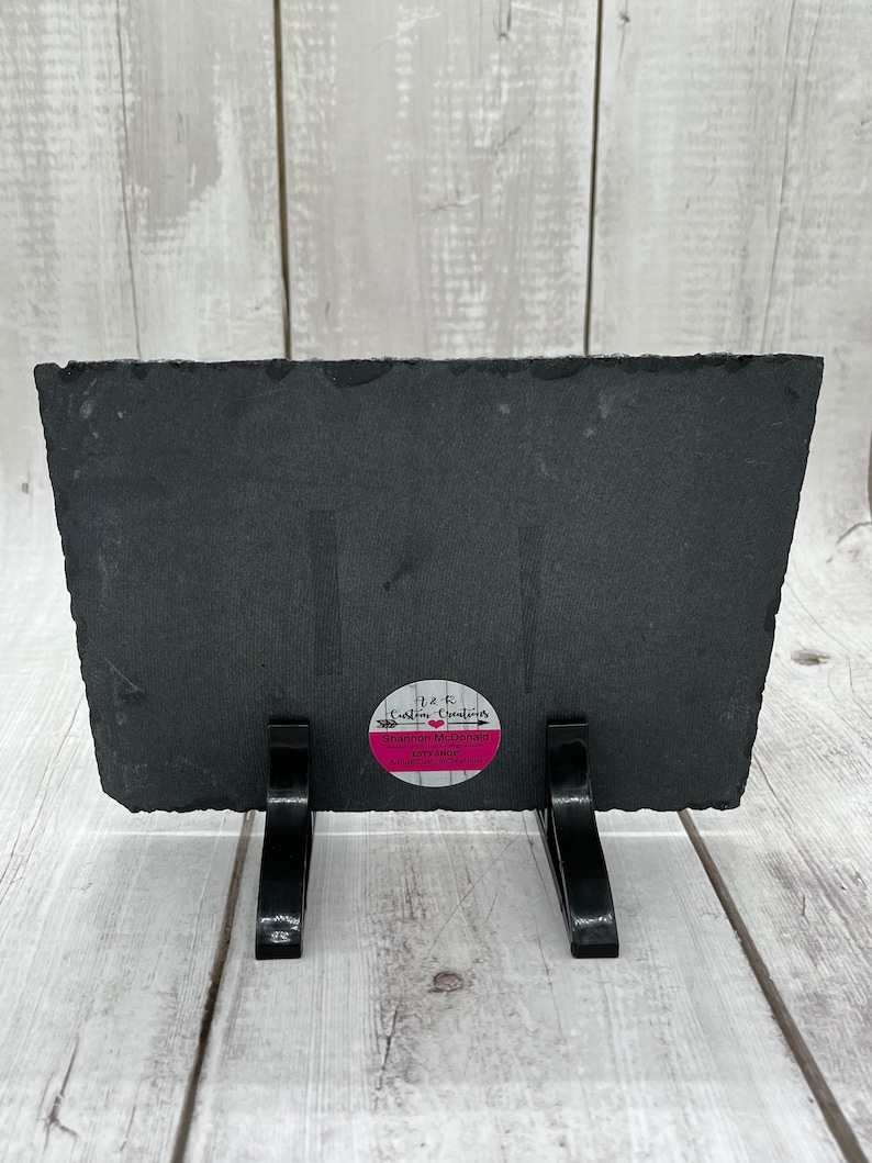 May include: Black slate plaque with a pink circle sticker that says "H&K Custom Creations, Shannon McDonald, Etsy Shop, Handmade with Love". The plaque is on a black stand with two legs.
