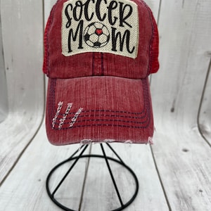 May include: Red and blue distressed baseball cap with a white patch that says "soccer mom" with a black soccer ball and a red heart.