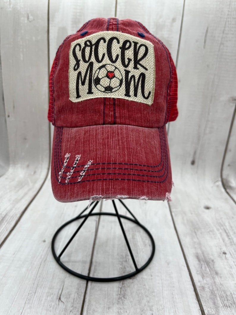 May include: Red and blue distressed baseball cap with a white patch that says "soccer mom" with a black soccer ball and a red heart.