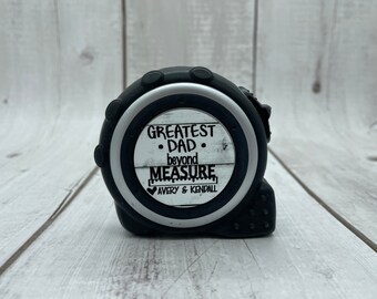 May include: Black and silver tape measure with a white label that reads "Greatest Dad. Beyond Measure. Avery & Kendall".