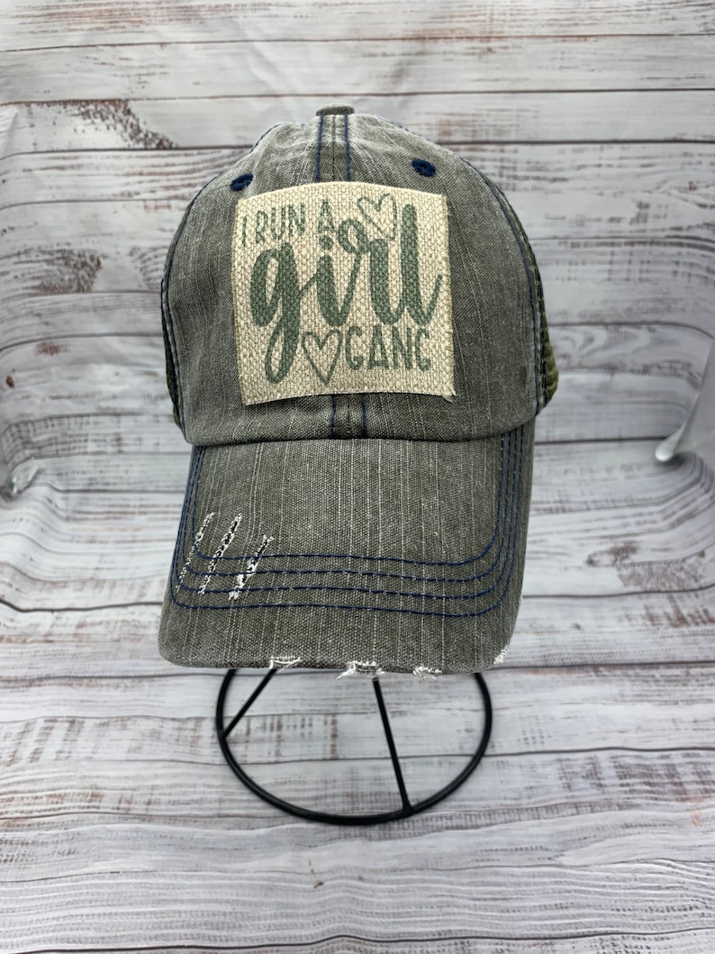 May include: A gray and blue distressed baseball cap with a patch that reads "I run a girl gang" in green lettering with a heart symbol.